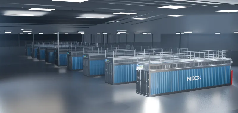 Rows of blue MDCX containers standing on the bare floor of a lit warehouse hall, each topped with a railed maintenance walkway — the pad is the footprint.